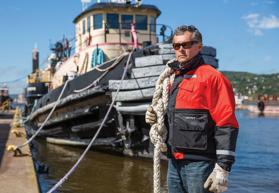 Man wearing a red and black Deluxe Flotation Jacket made by Kent Safety Products standing infront of a boat with Docking Line thrown over his shoulder.