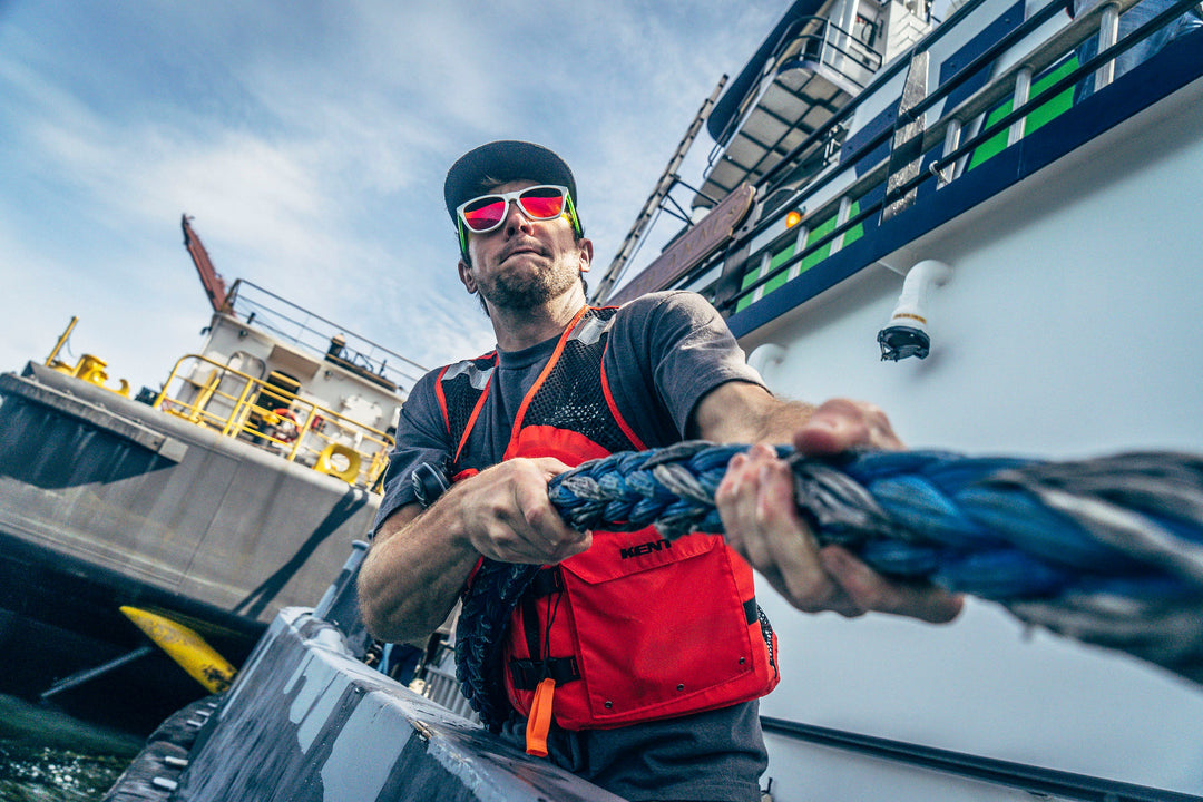 A worker wearing a red Kent Safety Products work Life Vest on a boat pulling Dock Line in a port.