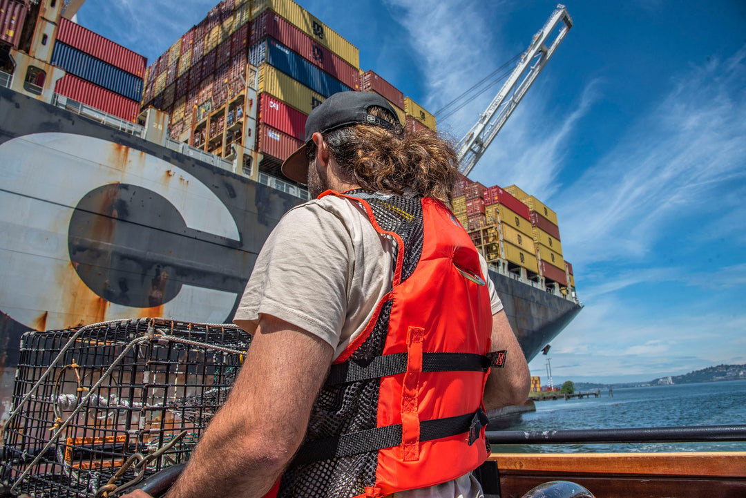 A port worker wearing a red Kent Safety Products Life Vests standing in front of a large shipping container ship.
