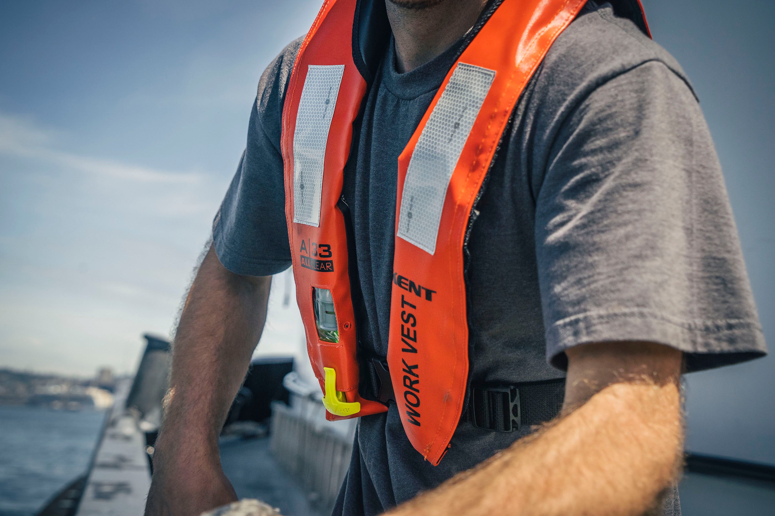 Person in orange life vest on a boat, handling a rope.