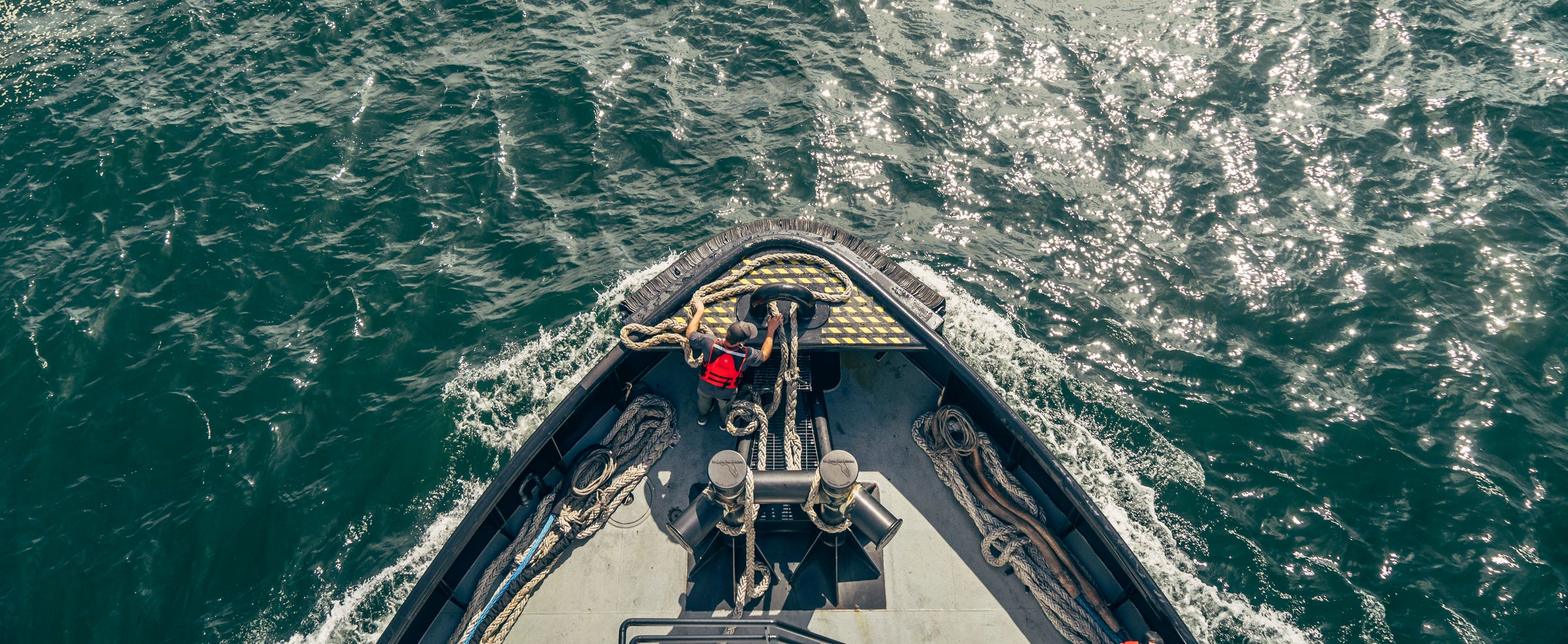 Aerial view of two people on a boats bow navigating through choppy water.
